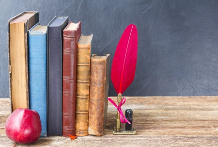 Wooden bookshelf  with  old books, apple  and red feather penの写真素材