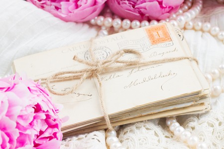 fresh pink  peonies with pile of old mail and pearl jewelery