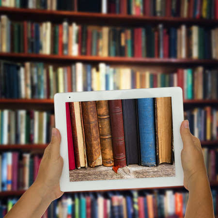 Hands holding  tablet with row of books on screen, library shelfs in background, e-learning concept