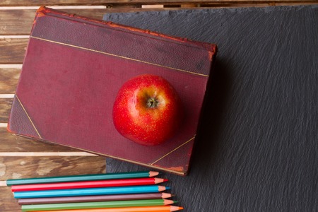 Set of colorful pencils with old book and red apple on black boardの写真素材