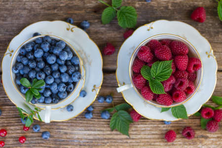 fresh raspberry and blueberry with green leaves in cups, top viewの写真素材