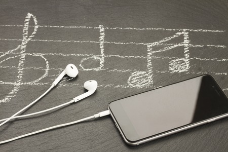 Music notes with treble clef, modern smartphone  and headphones
