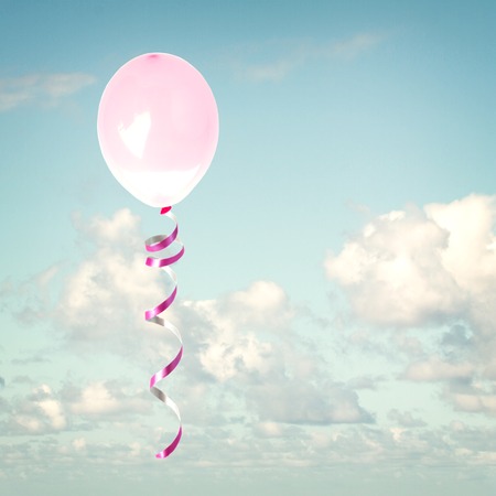 one pink birthday baloon in the cloudy blue skyの写真素材