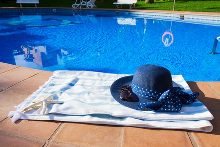 towel and summer hat  near pool at sunny summer day