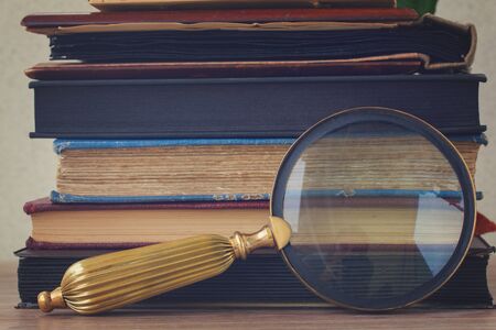 pile of vintage old books stacked on table with  looking glass, retro tonedの写真素材