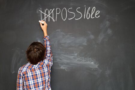 boy putting a cross over impossible on blackboardの写真素材