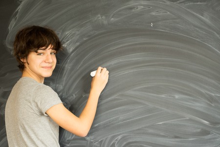 Boy with chalk in hand writting on empty black boardの写真素材