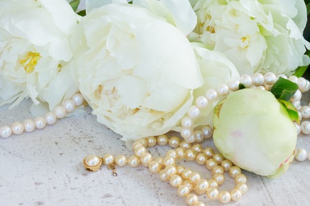 White fresh peony flowers with pearls jewellery on white wooden tableの写真素材