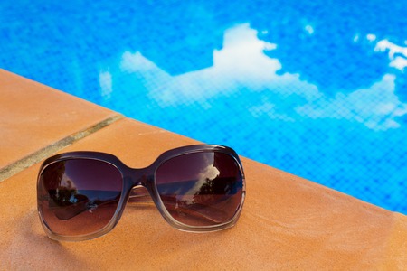 Sunglasses near blue tiled water of poolの写真素材