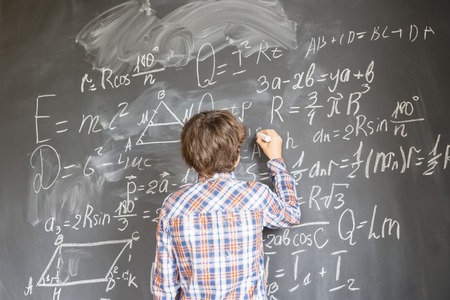 Boy with chalk writting on math formulas black board
