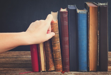 Hand taking book from wooden bookshelf with row of antique books, retro tonedの写真素材
