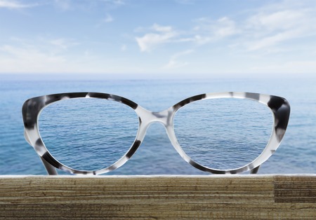 hipster glasses on a wooden table in front of the seaの写真素材