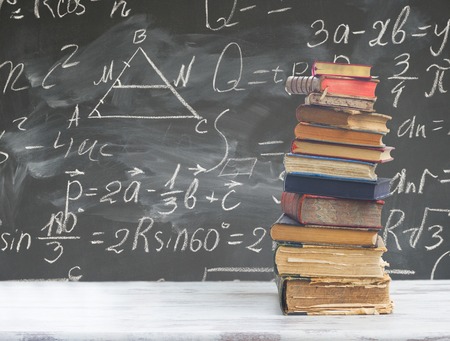 stack of books on white wooden table with math formulas on blackboardの写真素材
