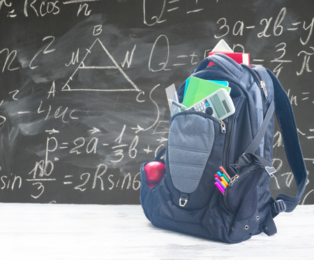 School backpack with supplies on white desktop, blackboard with math formulas in backgroundの写真素材