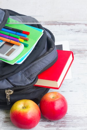 School backpack with supplies and two apples on white desktop close upの写真素材