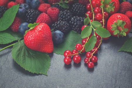 fresh berries with green leaves on black stone background, retro tonedの写真素材