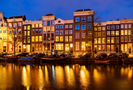 Typical dutch houses over canal with reflections illuminated at night, Amsterdam, Netherlandsの写真素材