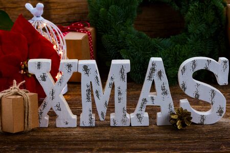 White Xmas wooden letters close up with fir tree wreath in background on wooden tableの写真素材