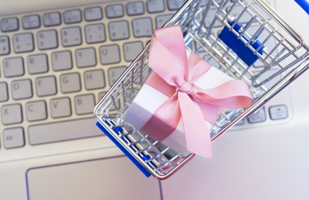On-line shopping concept - shop cart with giftbox and laptop keyboardの写真素材