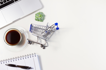 On-line shopping concept - lapytop keyboard, shopping cart and coffee, copy space on white tableの写真素材
