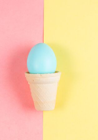 Conceptual easter blue painted egg in cone on yellow and pink background