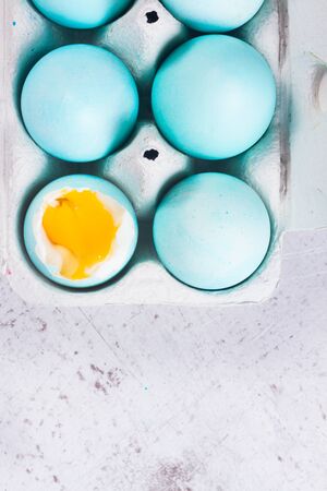 Set of blue easter eggs, one with yolk, top view on white aged tabletop close up