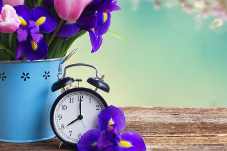 Spring time concept - retro alarm clock with flowers copy space on blue bokeh backgroundの写真素材
