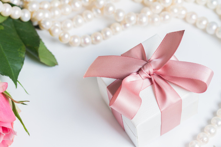 Gift box with pink ribbon with pearl jewellery on white tableの写真素材