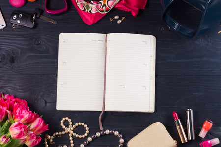 female flat lay scene - fresh flowers and accessories on black wooden background with copy space on white open ntebookの写真素材