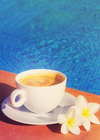 white cup of coffee near pool blue water with copy spacer, retro tonedの写真素材