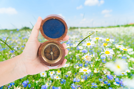 Someones hand holding old vintage compass, summer meadow in background