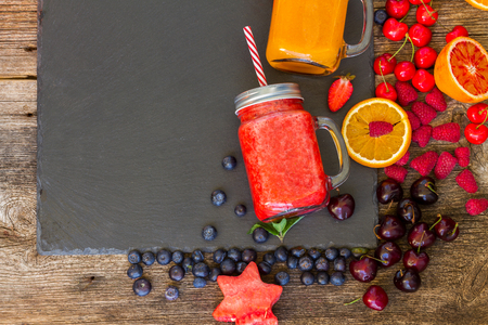 Fresh smoothie citrus and red berry drinks with igredients, copy space on black stoneの写真素材