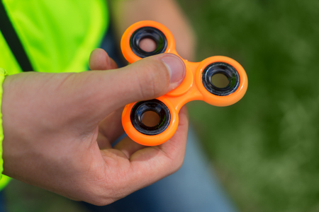 trendy fidget spinner - person holding orange fidget spinner in hand, close up viewの写真素材