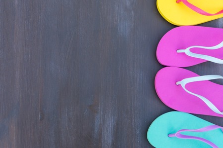 Summer beach fun - border of flip flop sandals, copy space on dark wooden background