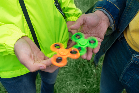 trendy fidget spinner - two persons holding spinning green and orange fidget spinners in hands, close up above viewの写真素材