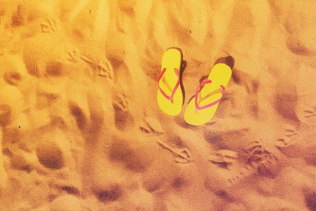 Summer beach fun - yellow flip-flops with seagull footprints on beach sand, retro tonedの写真素材
