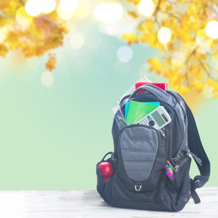 School backpack full of supplies on white desktop, fall leaves backgroundの写真素材