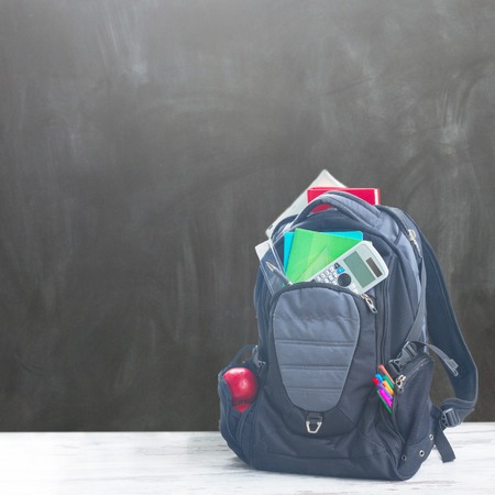 School backpack full of supplies on white desktop in classroom, copy space on blackboardの写真素材