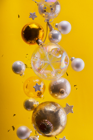 Silver and golden christmas bubbles and stars flying on yellow background, christmas magic conceptの写真素材