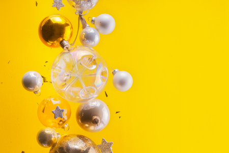 Silver and golden christmas bubbles and stars flying on yellow background with copy spaceの写真素材