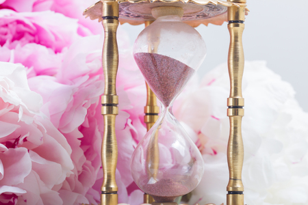Hour glass and fresh peony flowers on white leather background