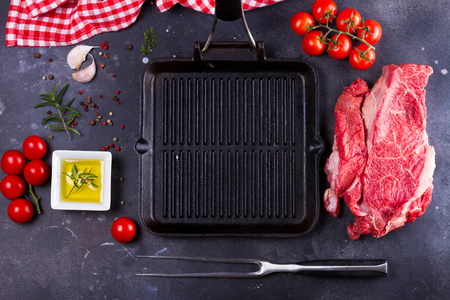Food background - spices, olive oil, meat fork, tomatoes and empty black panの写真素材