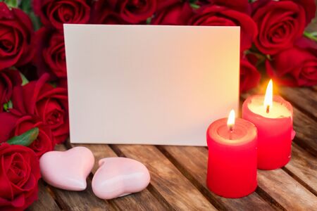 Two burning candles with fresh roses on wooden table, copy space on paper noteの写真素材