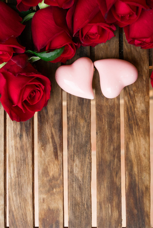 red fresh roses with two pink hearts on wooden tableの写真素材
