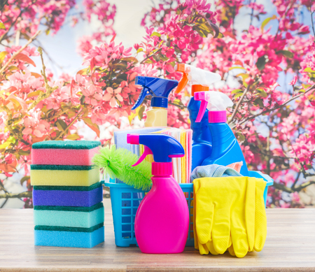 Spring cleaning concept - colorful sprays bottles and rubbers on wooden table over spring backgroundの写真素材