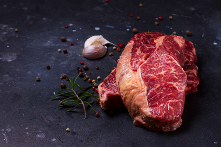 Raw beef steak with pepper and garlic on dark stone backgroundの写真素材
