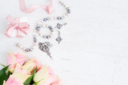 Present box with pink ribbon with jewellery and roses on white table, top view scene with copy spaceの写真素材