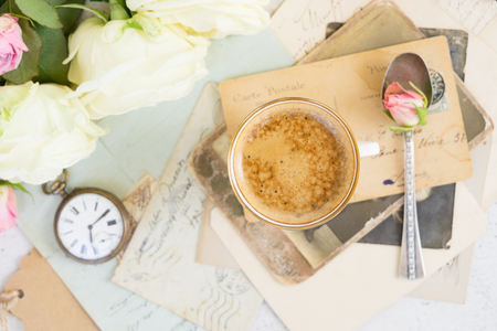 Pink and white roses with cup of fresh brewed coffee on pile of old mailの写真素材