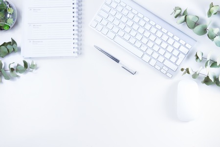 Flat lay home office workspace with white modern keyboard, notebook and silver green twigsの写真素材