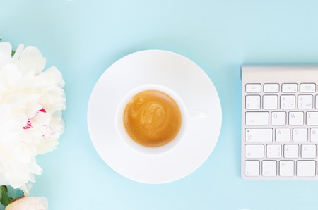 Flat lay home office workspace with cup of coffee, white modern keyboard and flowers
